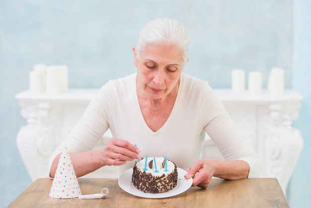 Senior Femme Solitaire Arrangeant Des Bougies Sur Un Gateau D Anniversaire A La Maison Photo Gratuite