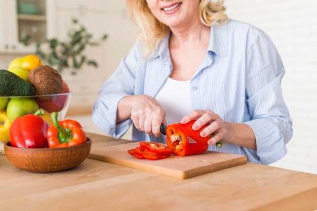 Senior femme souriante coupe le poivron rouge avec un couteau | Télécharger des Photos gratuitement