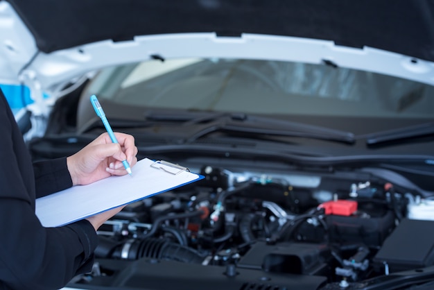 Service de voiture, réparation, concept de maintenance - mécanicien automobile asiatique ou smith écrivant dans le presse-papiers d'un atelier ou d'un entrepôt, technicien effectuant la liste de contrôle pour la réparation d'une machine neuve Photo Premium