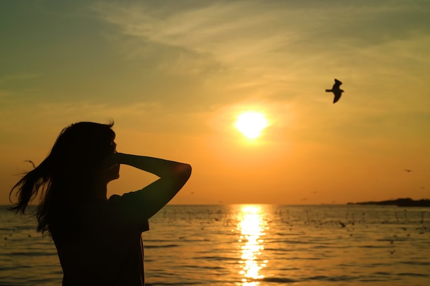 Silhouette De Jeune Femme En Regardant Le Soleil Levant Sur Un Ciel Dore Avec Un Oiseau En Vol Photo Premium