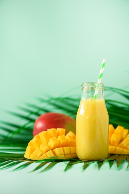 Smoothie Juteux Délicieux Avec L'orange Et La Mangue. Pop Art Design, Concept Créatif De L'été. Jus De Fruits Frais Dans Des Bouteilles En Verre Sur Des Feuilles De Palmier Vert. Photo Premium