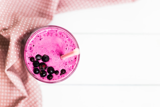 Smoothies banane et cassis dans un verre sur une table blanche à côté d'une serviette rose mouchetée avec une paille Photo Premium