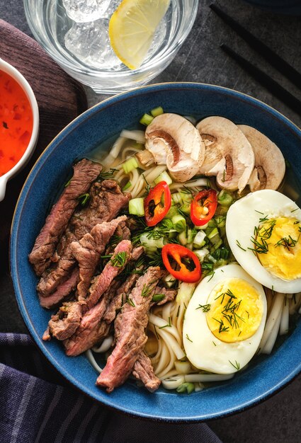 Soupe de ramen asiatique avec bœuf, œuf, ciboulette et champignons dans un bol. vue de dessus Photo Premium