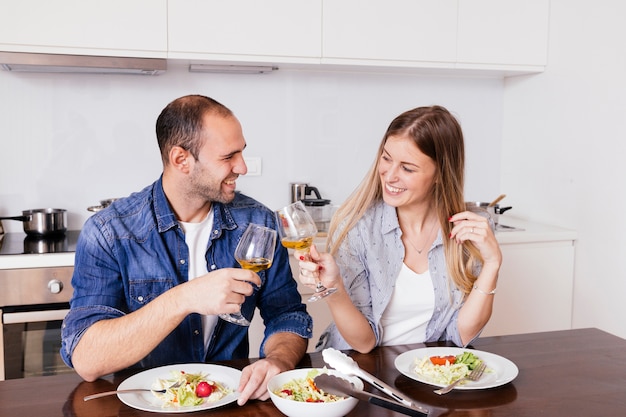 Souriant, jeune couple, manger, salade, grillage, à, verres vin, dans cuisine Photo gratuit