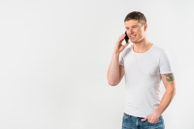 Souriant jeune homme parle au téléphone portable avec sa main dans la poche Photo gratuit