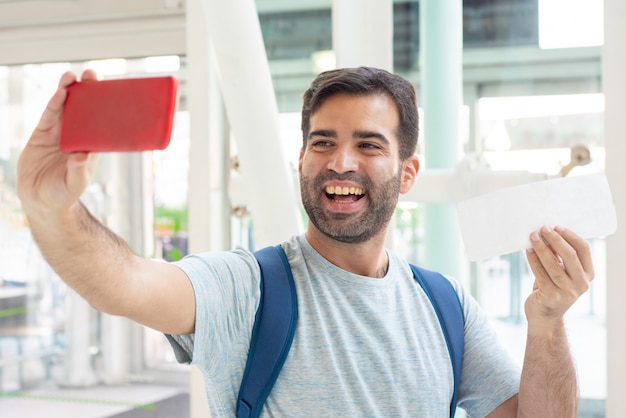 Souriant jeune  homme  prenant selfie  avec ticket 