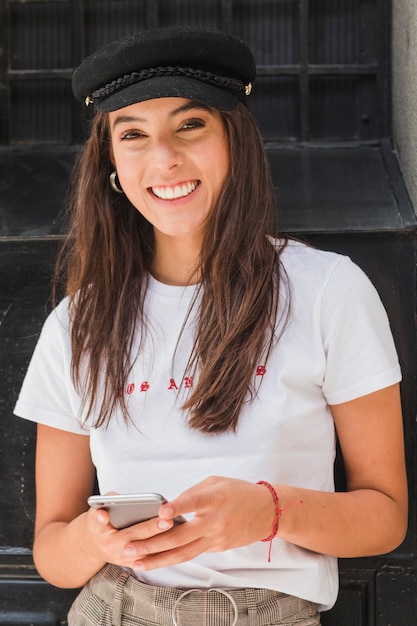 Souriant portrait d'une jeune femme tenant un téléphone portable à la main en regardant la caméra Photo gratuit