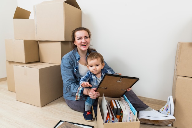 Souriante jeune femme avec son fils assis dans sa nouvelle maison avec des boîtes en carton Photo gratuit