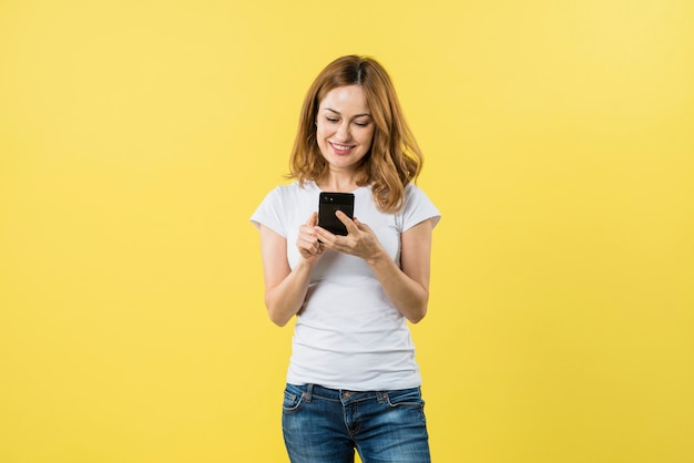 Sourire des messages sms jeune femme sur téléphone mobile sur fond jaune Photo gratuit
