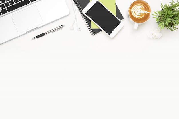 Table de bureau blanche avec ordinateur portable, smartphone, tasse de café et fournitures. Photo Premium