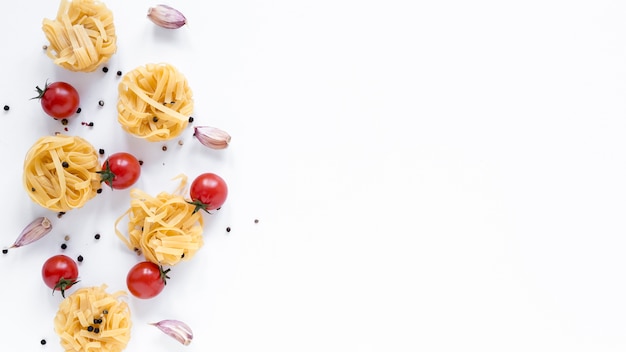 Tagliatelles non cuites; tomate cerise; gousse d'ail; poivre noir isolé sur fond blanc avec un espace pour le texte Photo gratuit