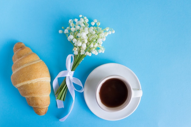 Tasse à café avec bouquet de fleurs de muguet et notes bonjour, beau petit déjeuner, vue de dessus, plat poser. croissant et café Photo Premium