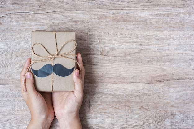 Tenant une boîte cadeau avec moustache sur fond en bois Photo Premium