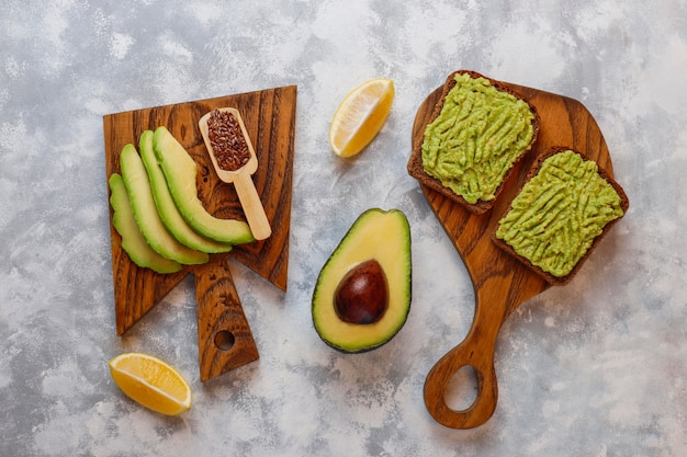 Toast ouvert aux avocats, tranches d'avocat, citron, graines de lin, graines de sésame, tranches de pain noir, vue de dessus Photo gratuit