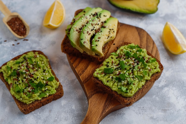Toast ouvert aux avocats, tranches d'avocat, citron, graines de lin, graines de sésame, tranches de pain noir, vue de dessus Photo gratuit
