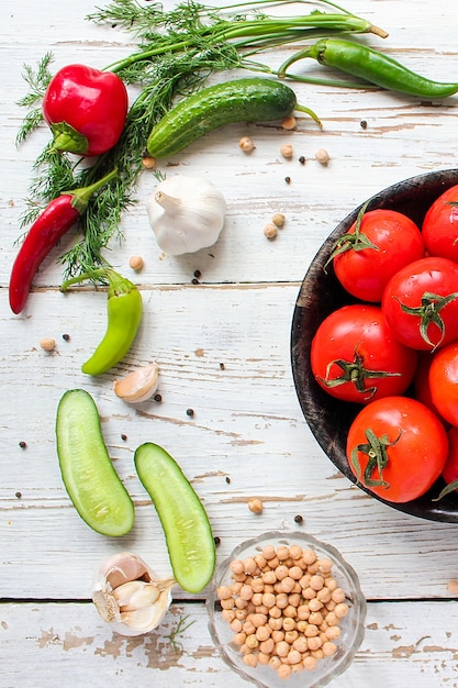 Tomates rouges biologiques fraîches dans une plaque noire sur une table en bois blanche avec des poivrons verts et rouges et rouges, des poivrons verts, des grains de poivre noirs, sel, gros plan, concept santé Photo gratuit