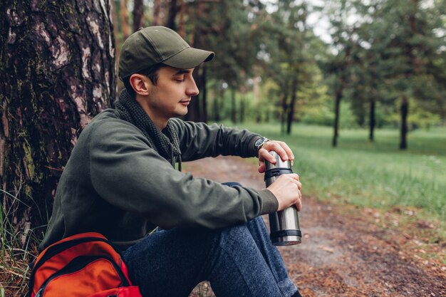 Tourisme homme ouvre thermos avec thé chaud dans la forêt de printemps camping, voyager Photo Premium