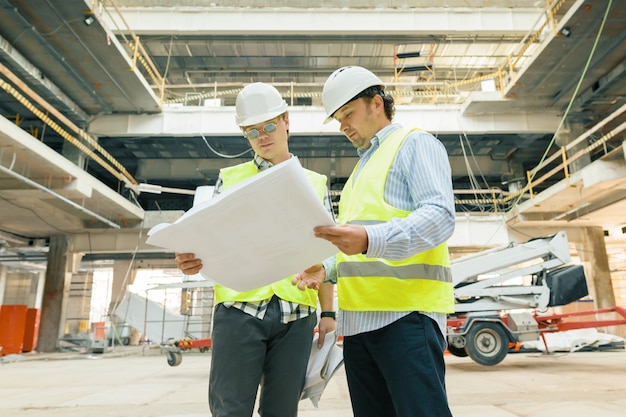 Les Travailleurs De La Construction De Sexe Masculin Travaillant Au Chantier De Construction Les Constructeurs A La Recherche De Plan Directeur Photo Premium