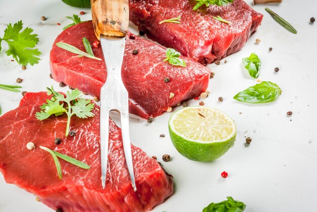 Viande Crue Fraîche. Filet De Boeuf, Steaks, Sur Une Table En Marbre Blanc. Avec De L'huile D'olive, Des épices Pour La Cuisson - Basilic, Romarin, Coriandre, Persil, Ail, Citron, Sel, Poivre. Espace Copie Photo Premium