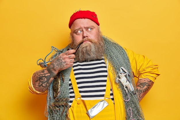 Vieux Marin Barbu Experimente Pense Au Lendemain En Mer Pose Avec Des Engins De Peche Fume La Pipe Habille En Salopette Chapeau Rouge Photo Gratuite