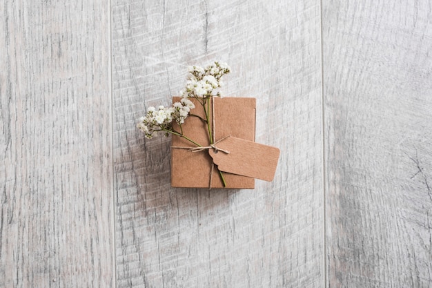 Vue aérienne d'une boîte en carton nouée avec une étiquette et des fleurs d'haleine de bébé sur un bureau en bois Photo gratuit