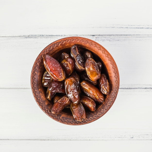 Une vue aérienne de dates dans un bol en bois sur une table en bois blanche Photo gratuit