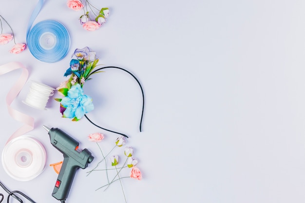 Une vue aérienne du ruban bleu et blanc; fleur artificielle; pistolet à colle pour la fabrication d'un serre-tête sur fond blanc Photo gratuit
