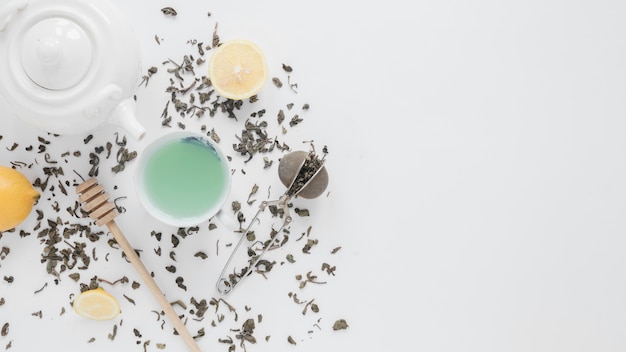 Une vue aérienne de feuilles de thé sèches; passoire à thé; citron; thé vert; louche de miel et théière sur fond blanc Photo gratuit