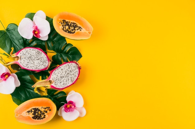 Une vue aérienne des fruits du dragon; papaye coupée en deux avec feuilles et fleur d'orchidée sur fond jaune Photo gratuit