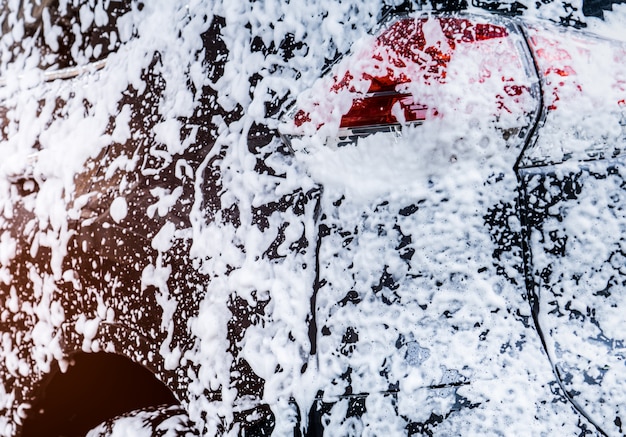 Vue arrière de la voiture suv compacte noire au design sportif et moderne lavée à l’eau et à la mousse blanche. Photo Premium