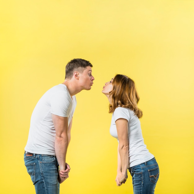 Vue côté, de, a, jeune couple, debout, face à face, soufflant bisous, sur, fond jaune Photo gratuit