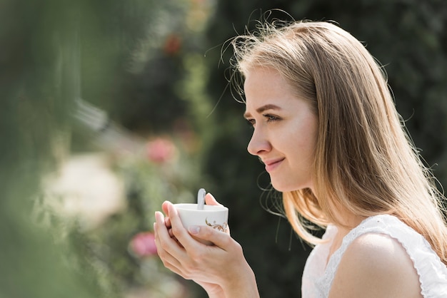 Vue de côté d'une jeune femme tenant une tasse de café à deux mains Photo gratuit