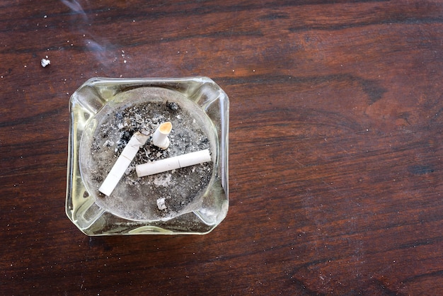 Vue de dessus de cigarettes bout à bout dans le cendrier sur une table en bois avec de la fumée de cigarette Photo Premium