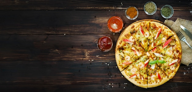Vue de dessus, dessus de pizza aux fruits de mer, et ingrédients, légumes à décorer tels que tomates, piments, champignons et ail. sur le fond de la table en bois. Photo Premium