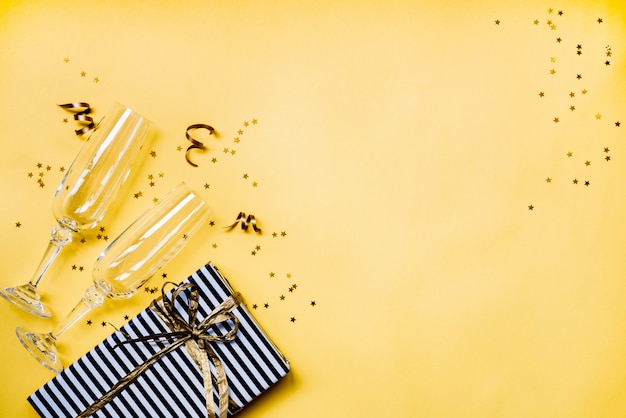 Vue de dessus de deux verres de champagne en cristal, une boîte-cadeau et des confettis dorés en forme d'étoile sur jaune Photo Premium