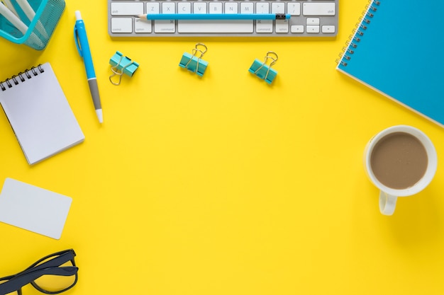 Une vue de dessus du clavier; lunettes et tasse de thé sur l'espace de travail jaune Photo gratuit