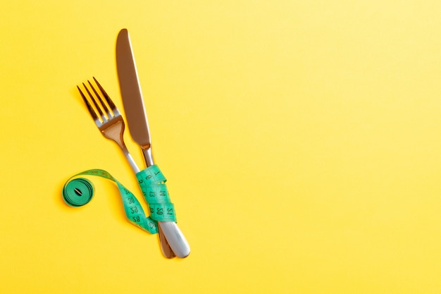 Vue de dessus des fourchettes et des couteaux en ruban à mesurer sur fond jaune. concept d'alimentation saine et de régime Photo Premium