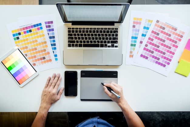 Vue de dessus d'un jeune graphiste travaillant sur un ordinateur de bureau et utilisant des échantillons de couleurs, une vue de dessus. Photo gratuit