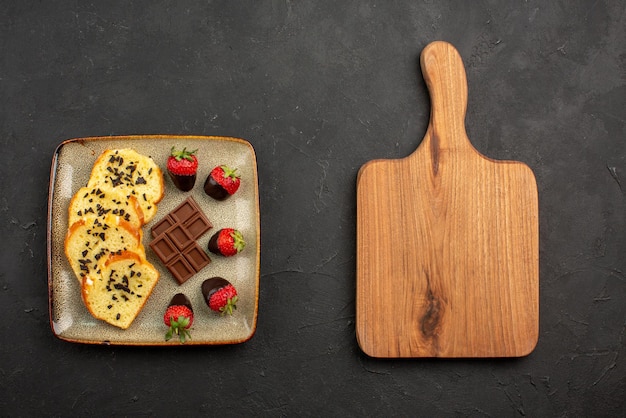 Vue De Dessus Des Morceaux De Gateau Appetissants Morceaux De Gateau Au Chocolat Et Aux Fraises A Cote De La Planche A Decouper En Bois Sur Une Table Sombre Photo Gratuite