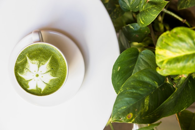 Vue de dessus de la mousse de thé vert matcha chaud sur un tableau blanc avec des feuilles vertes Photo gratuit