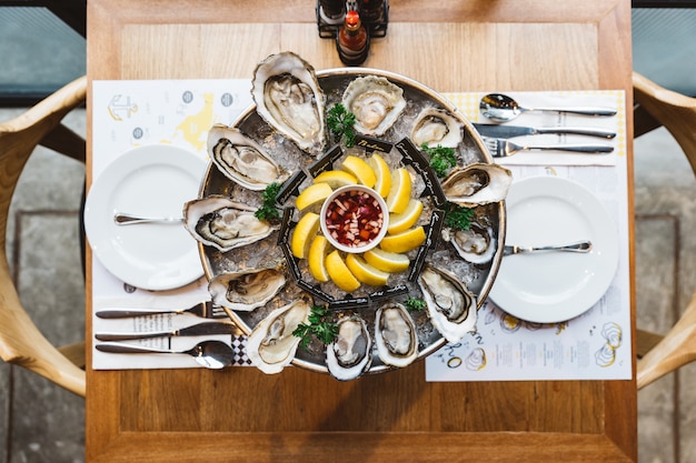 Vue de dessus de nombreux types d'huîtres fraîches servies dans un plateau rond avec une tranche de citron et une sauce épicée. Photo Premium