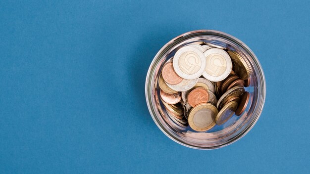 Une vue de dessus des pièces de monnaie dans le bocal en verre sur fond bleu Photo gratuit