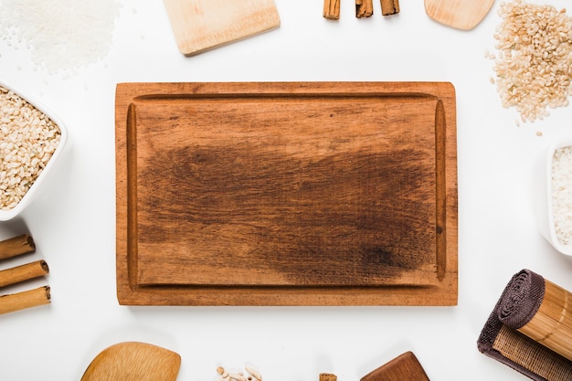 Une vue de dessus d'un plateau en bois vide avec une spatule; riz; bâtons de cannelle sur fond blanc Photo gratuit