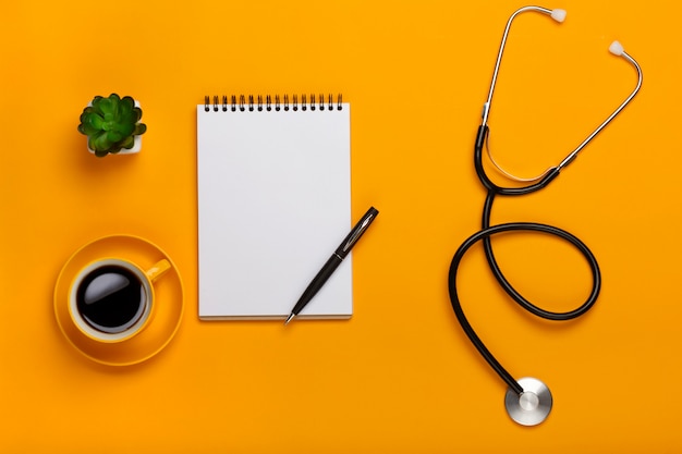 Vue De Dessus D'une Table De Médecin Avec Un Bloc-notes Et Un Stylo Stéthoscope, Un Clavier, Une Ordonnance Et Des Pilules, Une Tasse De Café Sur Un Fond Jaune Photo Premium