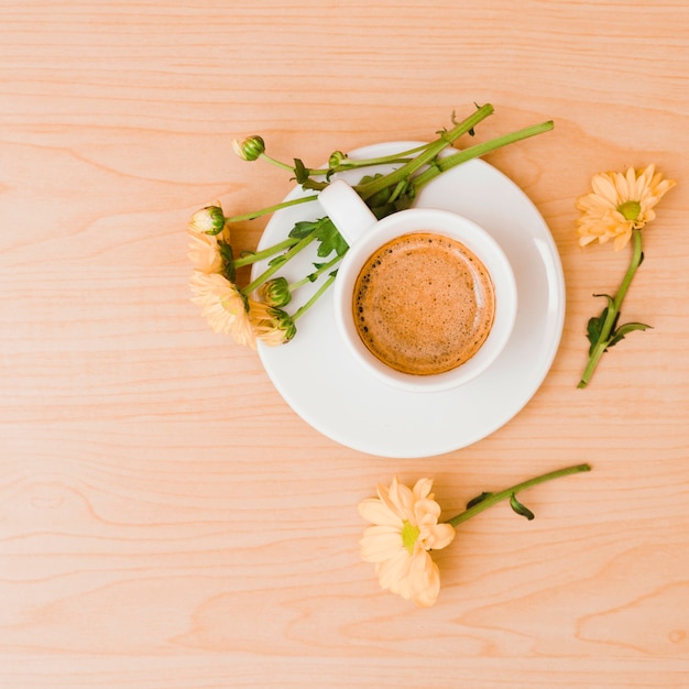 Une vue de dessus de la tasse à café et une soucoupe avec des fleurs couleur pêche sur fond texturé en bois Photo gratuit
