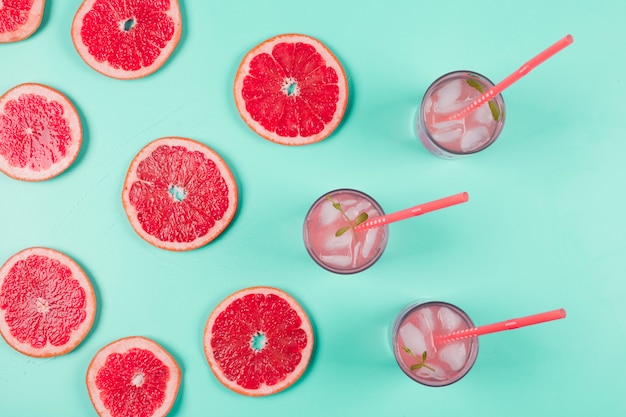 Une vue de dessus de tranches de pamplemousse et verre de jus avec glace et menthe sur fond pastel Photo gratuit