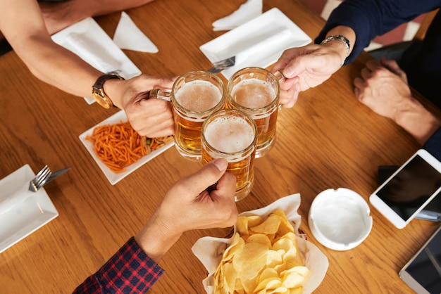 Vue de dessus de trois amis méconnaissables portant un toast avec des chopes à bière Photo gratuit