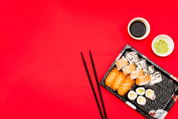 Une vue en élévation d'un plateau rempli de savoureux petits pains près de wasabi et de sauce de soja dans un bol sur une surface rouge Photo gratuit