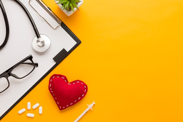 Vue élevée de lunettes; tablette; injection; en forme de cœur cousu; plante succulente; stéthoscope sur fond jaune Photo gratuit