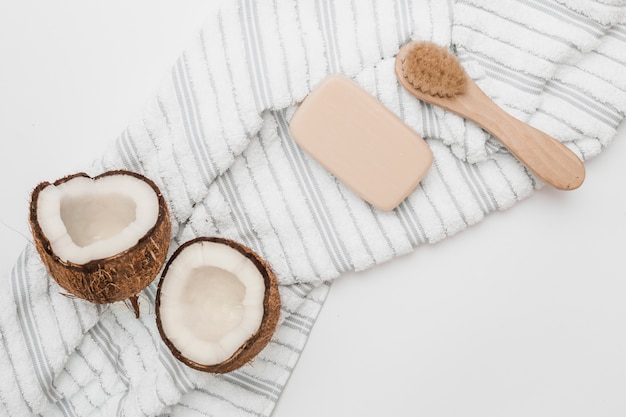 Vue élevée de la noix de coco coupée en deux; serviette; savon et pinceau sur fond blanc Photo gratuit